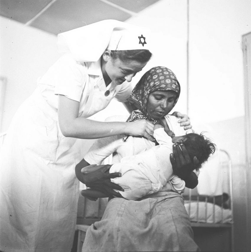 במעברת ראש העין, אחות מדריכה עולה חדשה מתימן כיצד להניק את תינוקה בבית התינוקות, 1949